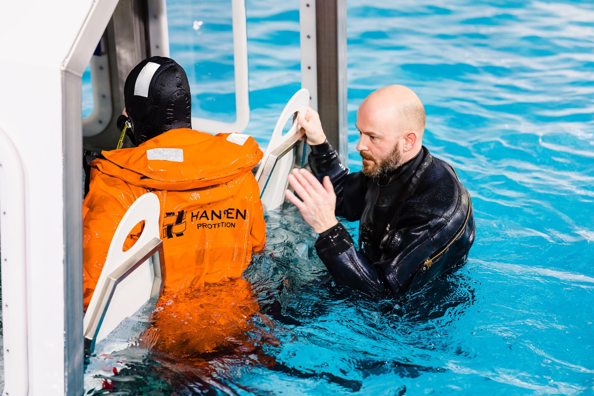 Instructor guiding a trainee through water evacuation procedures, focusing on practical skills for safety and survival in offshore conditions.