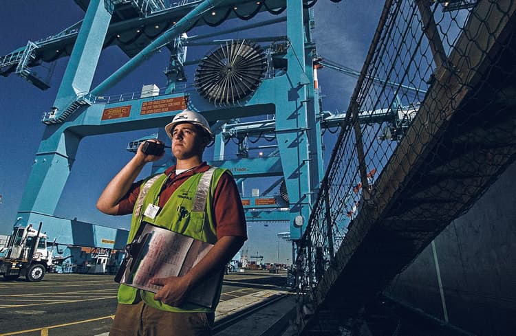 Port terminal worker coordinating crane operations, demonstrating safety and communication protocols in managing cargo logistics under the towering presence of large cranes