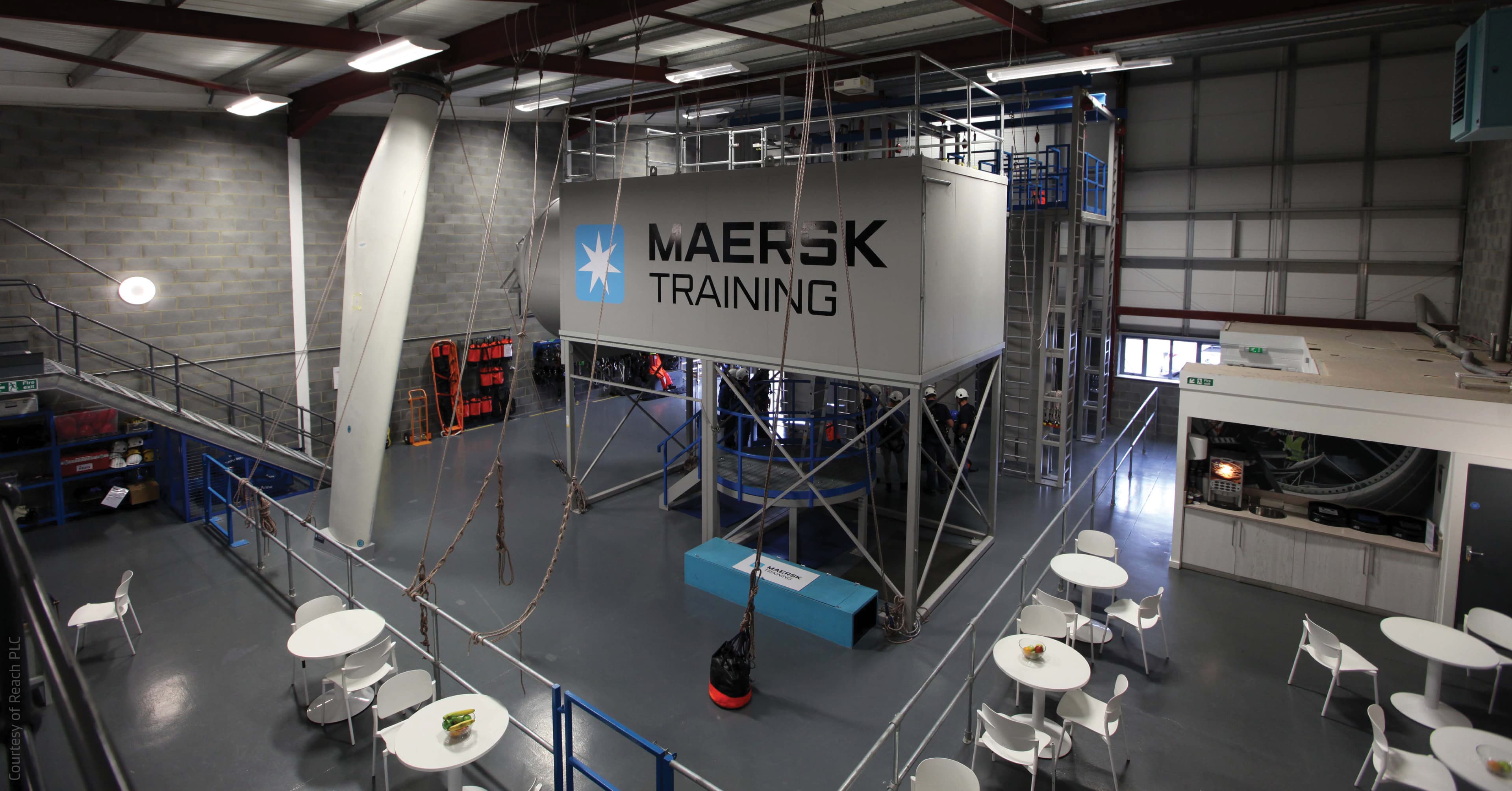 indoor training facility branded with "Maersk Training," featuring a high structure equipped for practical exercises, likely simulating industrial or maritime environments. The space includes seating areas, indicating a blend of training and collaborative zones.