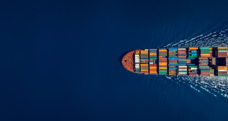 An aerial view of a container ship sailing through open waters, carrying multicoloured containers, symbolising global trade, logistics, and maritime transport efficiency.